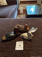 Four duck figurines displayed on a fabric surface including wooden, ceramic and crystal types