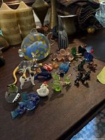 A variety of small colorful glass animal figurines including fish, dog, frog, birds, and others arranged on a surface.