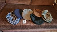 Overview of all five wool and tweed vintage hats laid out flat on a brown fabric sofa.
