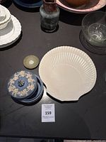 Overview of ceramic items including white shell dish, blue jasperware jar with lid, small bottle, glass bowl, and white scalloped plates