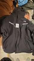 Black The North Face jacket laid out, showing front zipper and two zippered pockets.