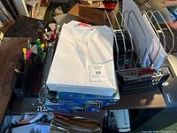 Top view of office supplies lot showing stacked reams of copy paper, desk organizers with pens, and wire file holders, electric stapler, and hole puncher