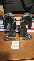 Pair of black marble horse head bookends side by side on wooden surface in front of stacked books.
