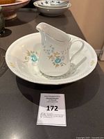 Porcelain pitcher inside a matching bowl, showing overall floral patterns and embossed details on bowl.