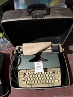 Teal Smith-Corona Electra 120 typewriter inside open black carrying case, with paper loaded and power cord visible.