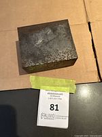 Top view of the solid metal ore block showing a roughly square shape and rusted surface texture on cardboard background.