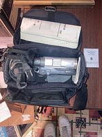 Sony Handycam DVD camcorder inside black carrying case with charger and manual visible.