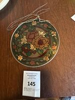 Round floral stained glass decor piece laying flat on wooden surface with attached hanging chain and wire