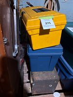 Stack of three toolboxes: yellow plastic toolbox on top, blue plastic toolbox in the middle, rusted metal toolbox on bottom