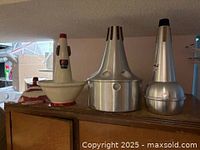 Photo showing three trombone mutes on a wooden surface: Jo Ral TRB-9 bucket mute, Humes & Berg 152 cup mute, Denis Wick DW5509 straight mute.