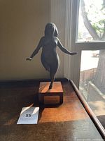 Front view of bronze statuette of nude female figure on wooden base