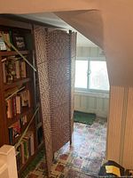 Full view of the three-panel wicker room divider standing open in a room with linoleum flooring and bookcases nearby.