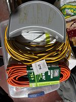 Two outdoor extension cords stacked in plastic container; yellow and black striped on top and orange packaged underneath.