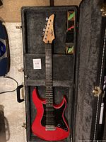 Open case view showing red guitar, pickguard, interior lining, strap