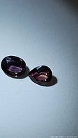Two faceted color change sapphires under daylight showing purple hues.