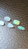 Five small faceted mixed cut natural Ethiopian opals with vibrant play of color on black leather background