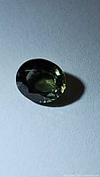 Oval cut green sapphire gemstone displaying deep green color and faceted surface with reflections under lighting.