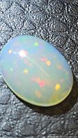 Close-up photo of the natural untreated Ethiopian opal oval cabochon showing rainbow flashes and galaxy pattern on a black textured background.