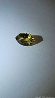 Close-up image of a single faceted chrysoberyl gemstone under lighting showing yellow-green hues and detailed facets.