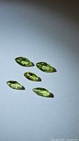 Five marquis cut natural apple green Peridot gemstones on a plain background, arranged in slight grouping showing the individual shapes and facets.