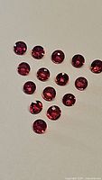Photo showing 14 small round faceted bright red rubies arranged loosely on white background.