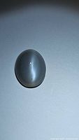 Photo of one oval cabochon moonstone showing strong cat's eye effect under direct illumination on a plain background.