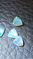 Three natural Ethiopian opal gemstones with triangular trillion cut, showing rainbow color flashes on black leather background.