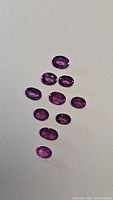 Eleven oval faceted rubies shown on white background, displaying shades from purple to red under natural lighting