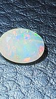 Close-up photo of the oval cut Ethiopian opal showing the multicolored flashes on a black textured background.