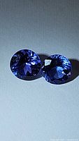 Two round deep blue faceted tanzanite stones side by side on a light background