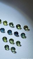 Photo showing 15 natural round cut green and blue sapphires of varying shades, approximately 2.5mm each