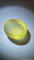 Oval lemon citrine cabochon gemstone showing deep golden yellow color with smooth polished surface under light, casting soft shadow.