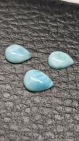 Three pear cabochon Larimar stones arranged on black textured background.