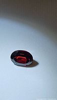 Oval cut garnet gemstone placed on a surface showing deep cherry red color with light reflections.