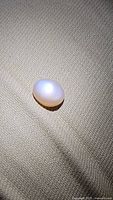 Oval cabochon cut peach moonstone gemstone placed on fabric, showing smooth surface and flash effect under lighting.