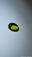 Oval cabochon cut natural Peridot gemstone photographed on a white background, showing vivid bright green color and polished surface.