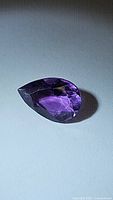 Photo of deep purple pear cut amethyst faceted gemstone on plain surface