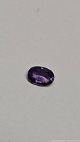 Oval cut purple sapphire gemstone on neutral background, showing color and clarity under daylight conditions