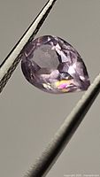 Close-up of pear cut pink purple amethyst held by tweezers showing the gemstone's facets and large rainbow internal inclusion.