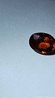 Oval cut spessartite garnet gemstone showing rich orange color and facet reflections against a plain background.