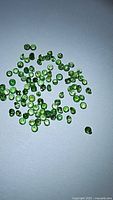 Photo showing a cluster of small, round cut, green tsavorite garnet gemstones on a white background.