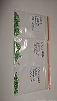 Photo of three clear plastic resealable bags each containing loose green gemstones labeled with carat weight and size range.