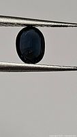 Close-up of the natural untreated blue spinel held by tweezers showing its oval cut and deep blue color under light.