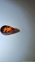 Pear shaped spessartite garnet gemstone with vibrant orange color photographed from an angle showing the side facets and depth.
