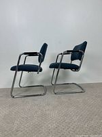 Side view of two cantilever chairs showing chrome frame and blue upholstery