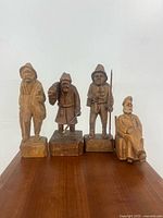 Four carved wooden folk art figures displayed side by side on a plain light background.