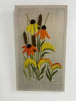 Close-up photo of hand-stitched floral crewel embroidery on a rectangular fabric panel.