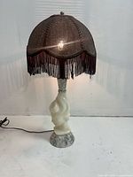Front view of vintage carved marble face lamp with dark tasselled fabric shade on white background.