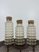 Front view of three smoked glass beehive canisters with cork stoppers on a decorative mat