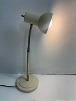 Full view of the vintage white metal gooseneck lamp illuminated against a plain background.